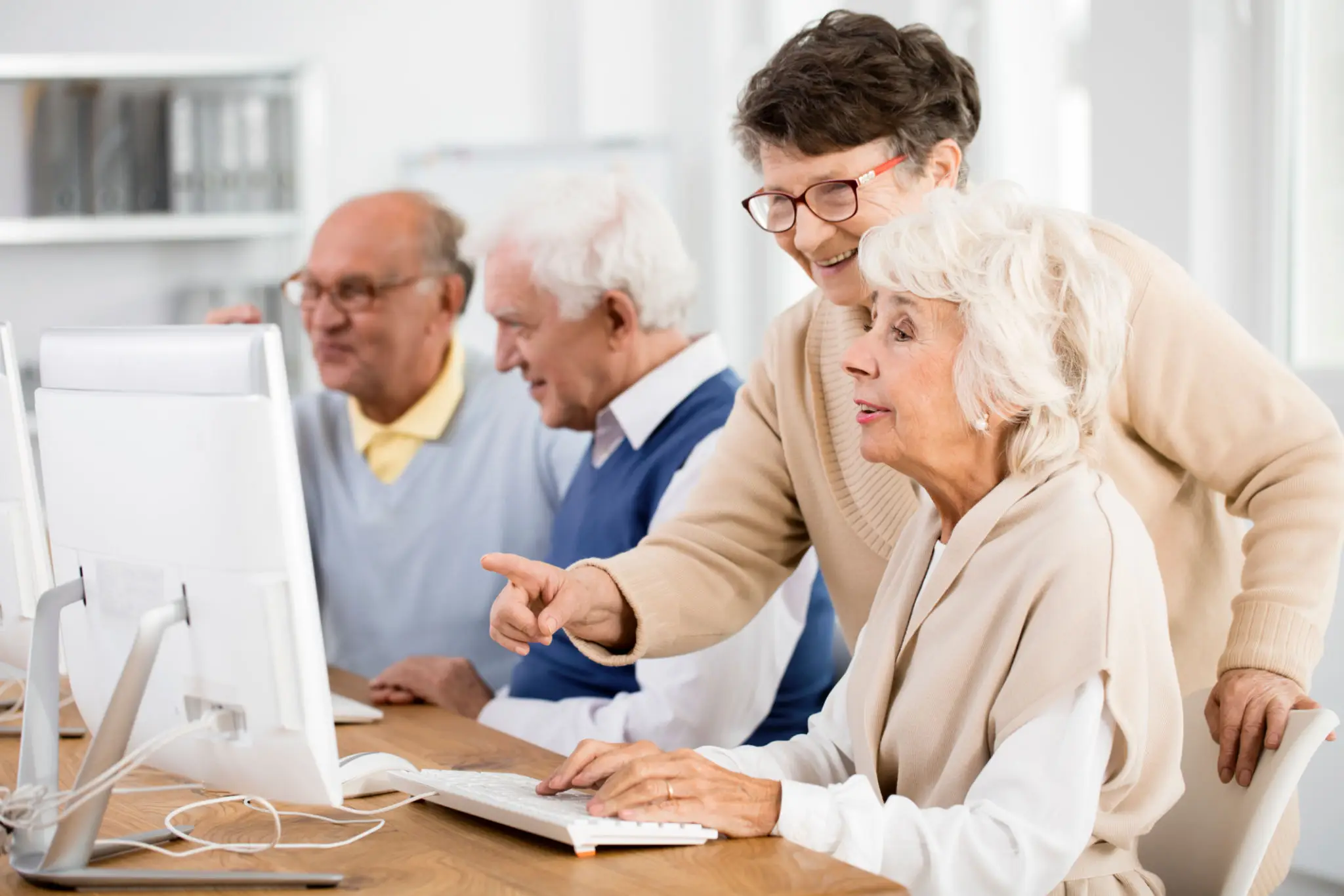 A young man assists seniors with a laptop in a bright room.