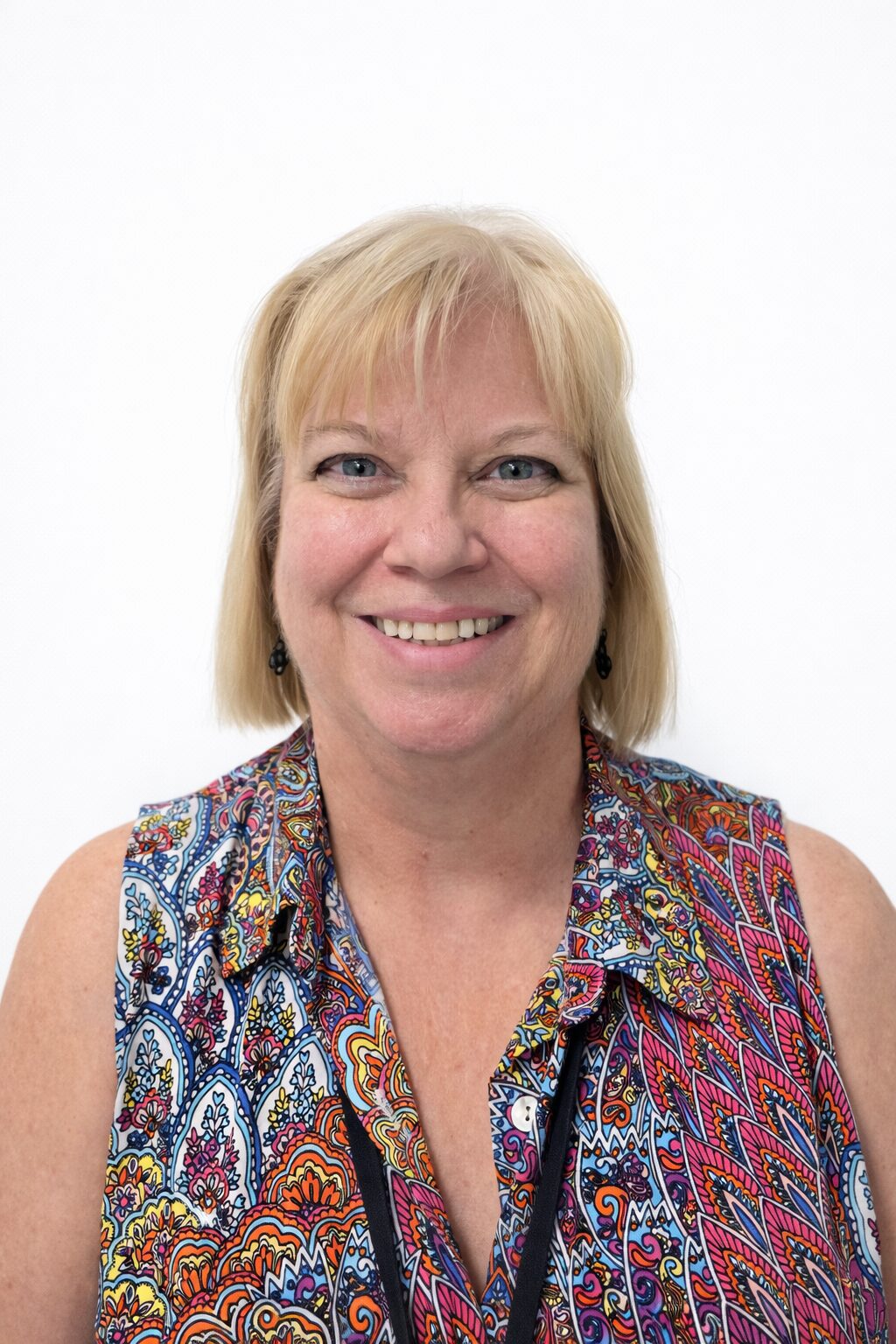 Smiling middle-aged woman with blonde hair wearing a colorful patterned sleeveless top.