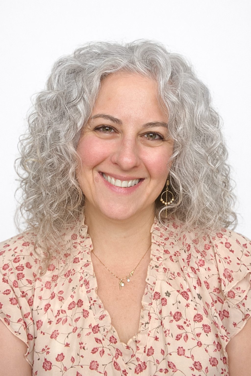 Smiling woman with curly gray hair and floral top.