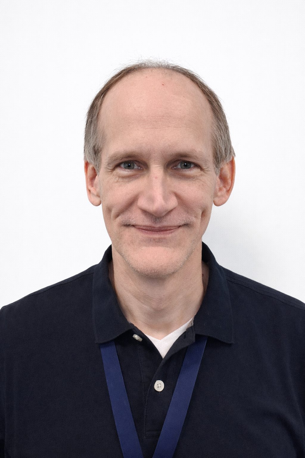 Smiling middle-aged man with a receding hairline in a dark polo shirt.