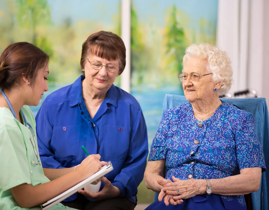 Two elderly women talking with a healthcare professional in a bright room.
