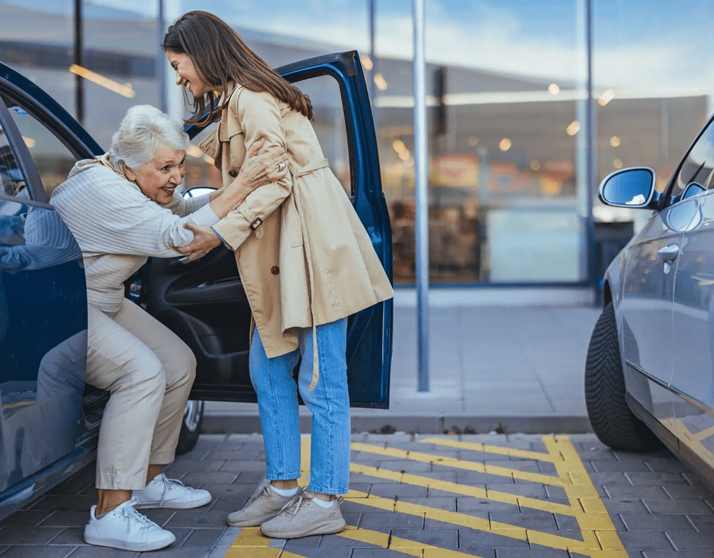 A young woman helping an elderly woman out of a car.