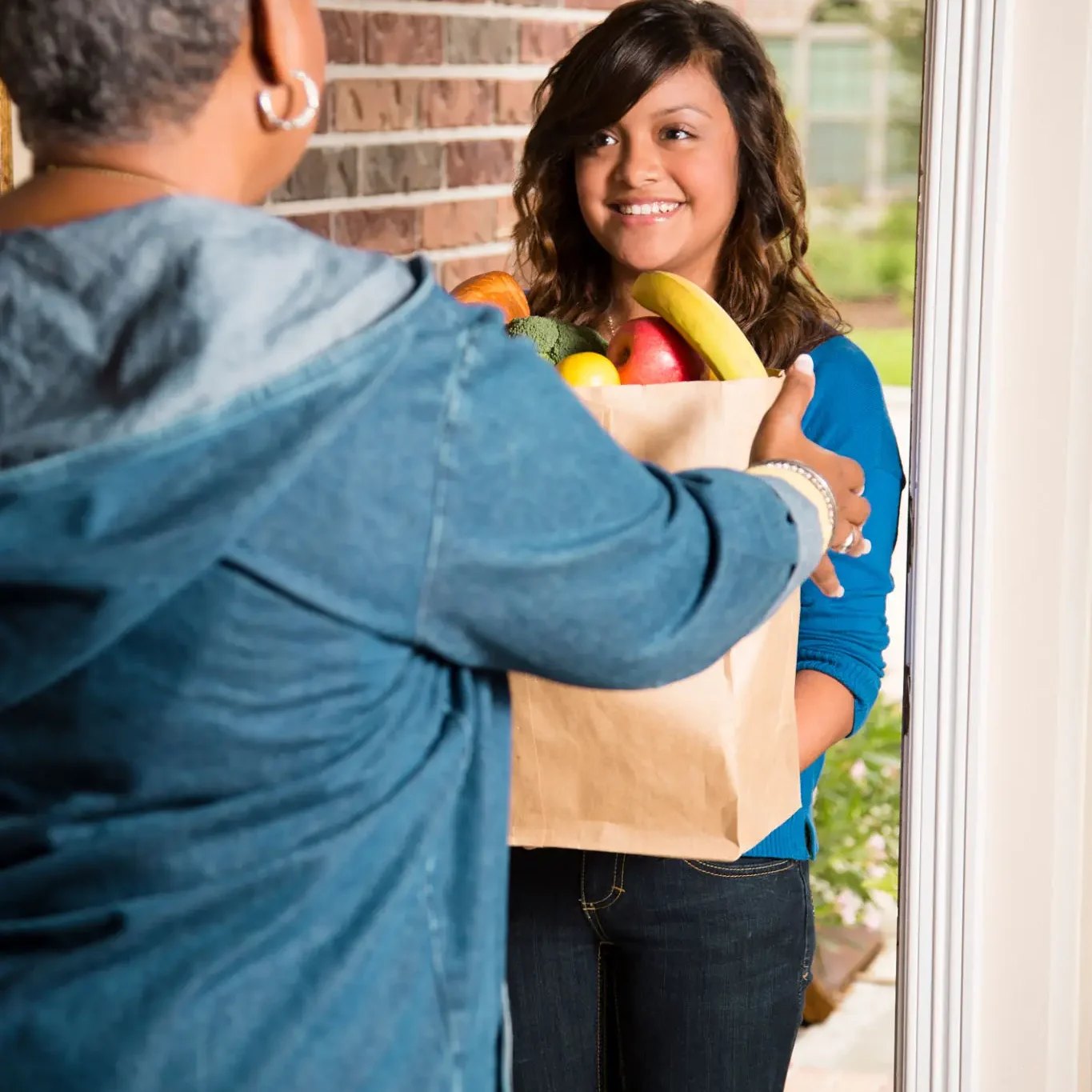 Man handing a grocery bag to a smiling woman at the door.