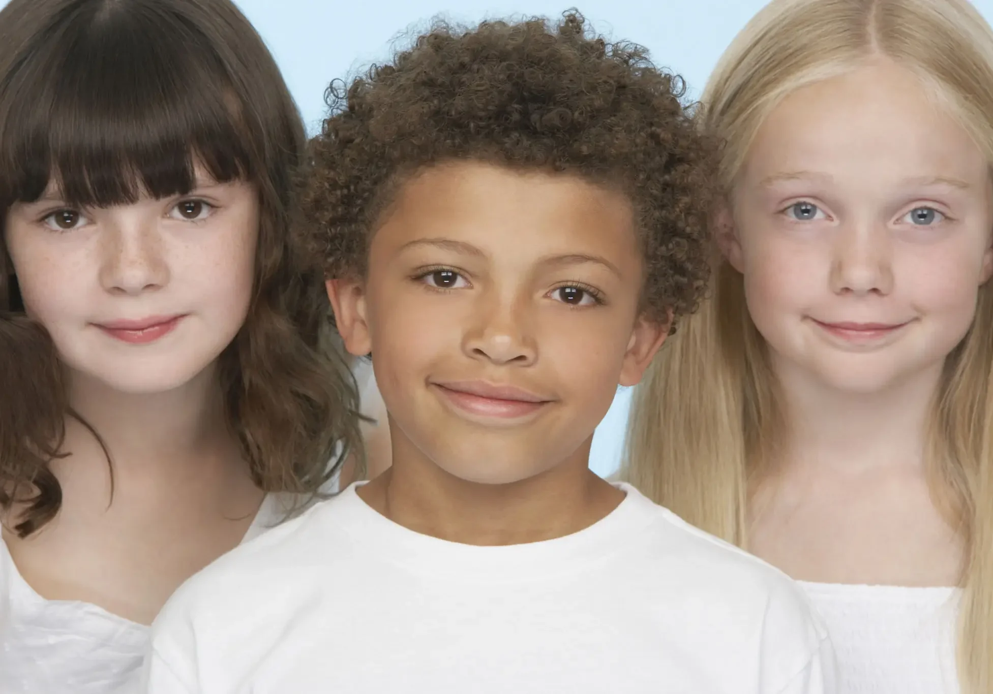 Three children smiling, standing closely together.